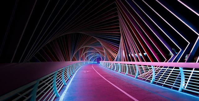 Colorful, illuminated bridge at night with vibrant, spiral-shaped LED lights creating a tunnel-like effect.